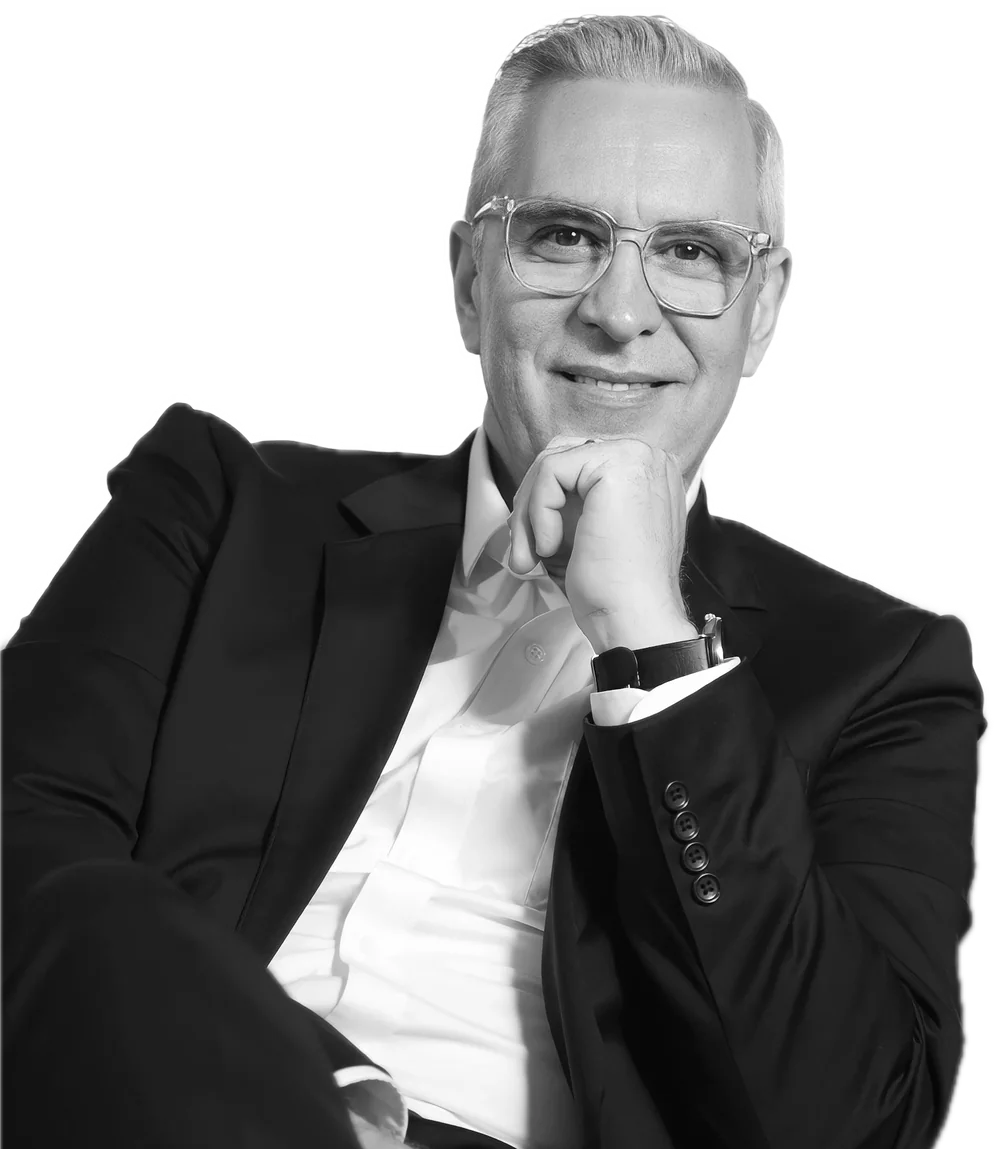 Un empresario de canas y gafas sonríe con la mano en el mentón.